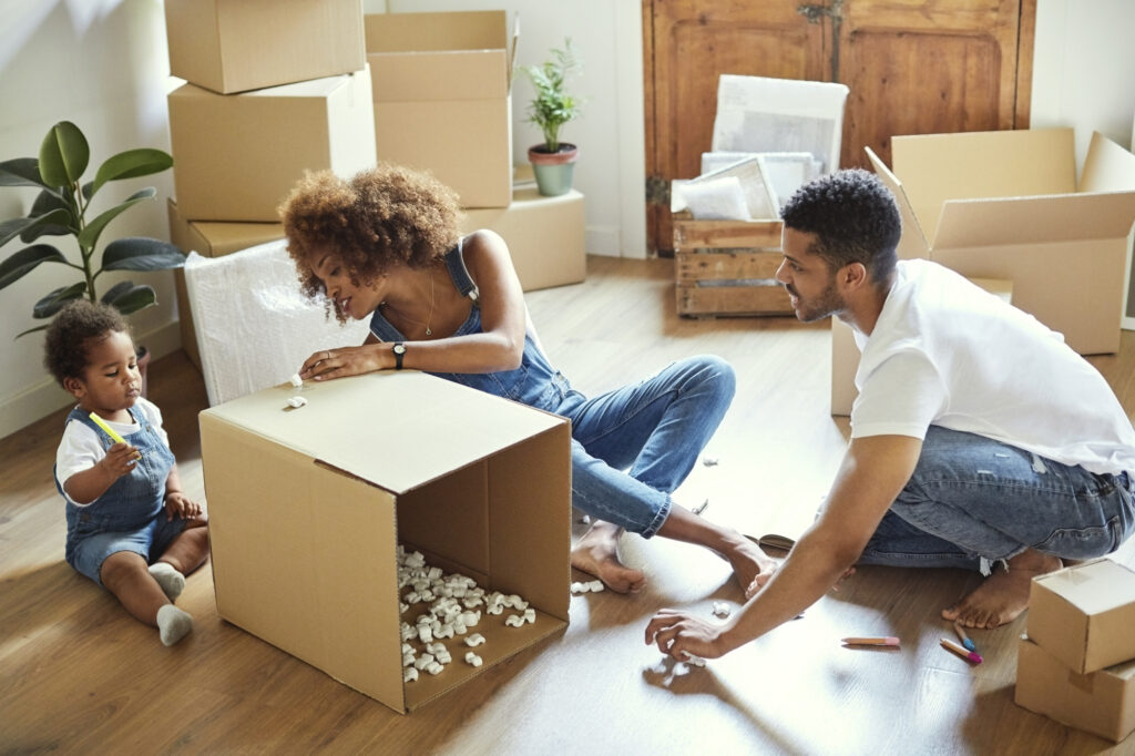 Une fillette dessine sur un carton tandis que ses parents sont assis par terre. Cette famille de trois personnes emménage dans un nouvel appartement. Ils sont en train de déballer les cartons chez eux.