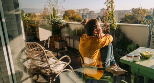 Photo d'une femme en train de boire son premier café du matin, de manger un plat à emporter et de lire les actualités du jour en ligne, sur le balcon de son appartement, tout en profitant du soleil printanier
