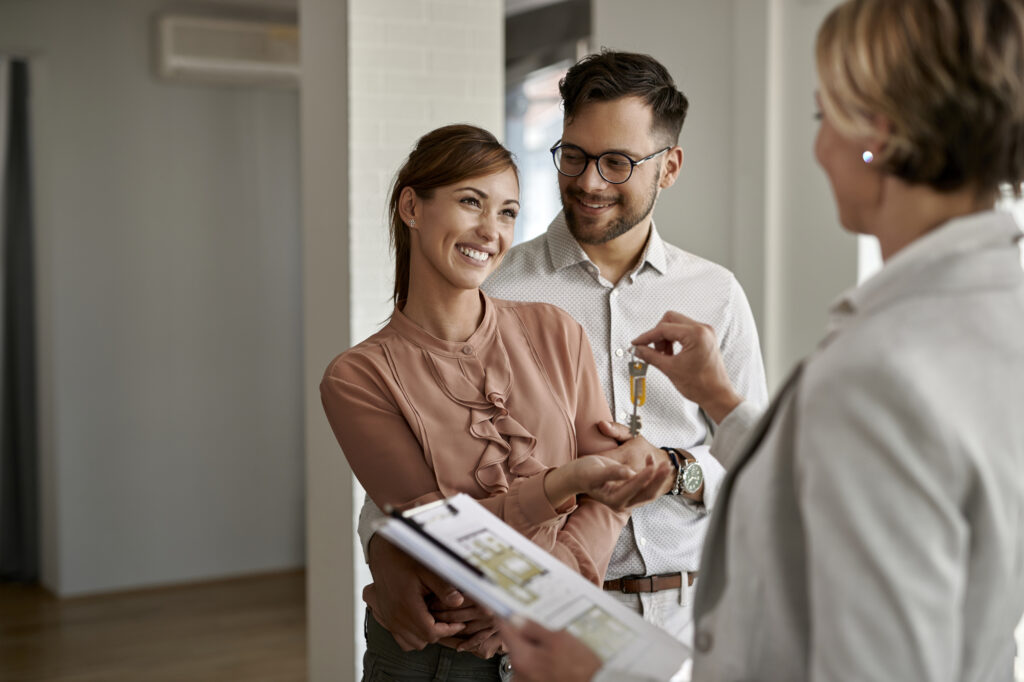 Un couple heureux achète une nouvelle maison et reçoit les clés des mains de l'agent immobilier.