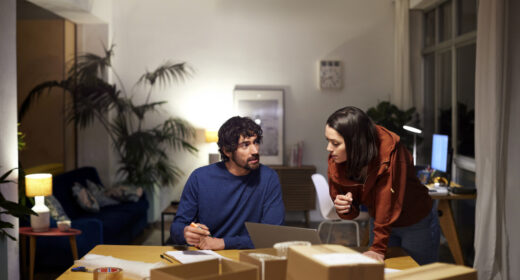 Male and female entrepreneurs discussing in illuminated apartment. Business colleagues are planning strategy. They are working late at home office.