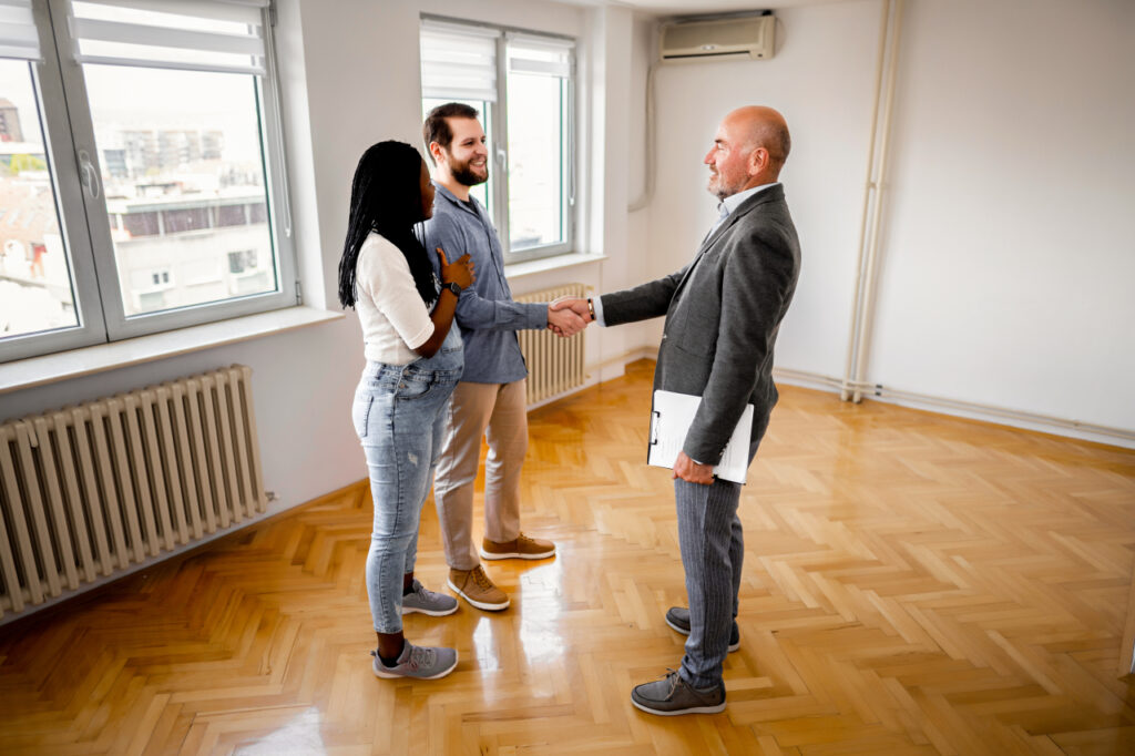 Male real estate agent shaking hands after making a deal with newlywed couple