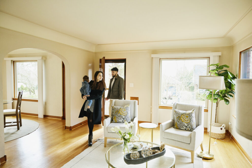 Wide shot of family with toddler walking though front door into living room of home for sale during open house